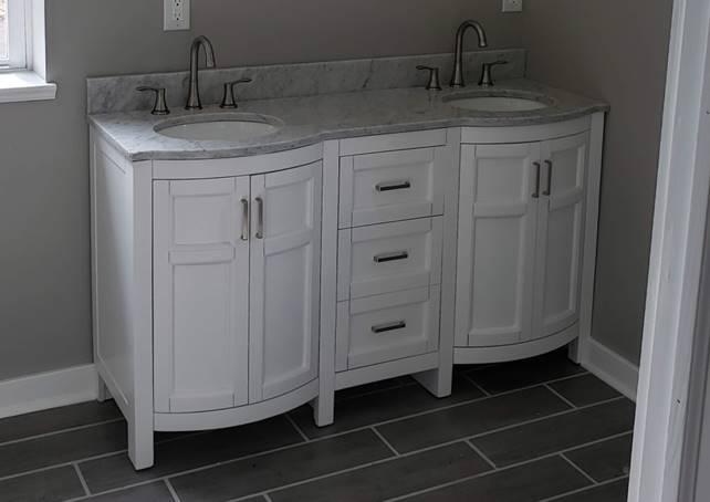 Double sink marble vanity with white cabinet doors, expertly installed by Applause Plumbing and Heating.  Applause Plumbing transforms outdated spaces into beautiful, functional havens. Meticulous attention to detail, upgraded plumbing fixtures, and thoughtful lighting create a warm, inviting atmosphere. Trust us to bring your bathroom dreams to life with professionalism, reliability, and a commitment to customer satisfaction.